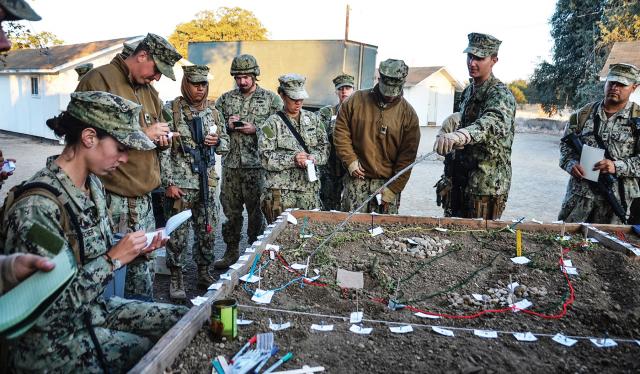 Intelligence professionals should embrace visual aids with three dimensions to make their presentations more dynamic and interactive, similar to the way this naval construction battalion is using a terrain model to brief sailors about the day’s mission during a field training exercise.